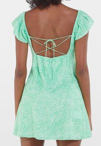 Light green dress with a speckled pattern. Features flutter sleeves and an open back with a crisscross tie detail. A-line silhouette, knee-length.