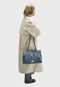 Borsa tote in denim con due manici robusti, forma rettangolare e design cucito. Presenta un'etichetta piccola sul davanti.