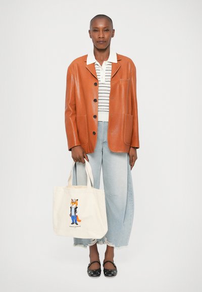 Blazer de cuero marrón, blusa blanca a rayas, jeans de pierna ancha desgastados, zapatos planos negros. Bolso tote beige con una ilustración de un zorro.