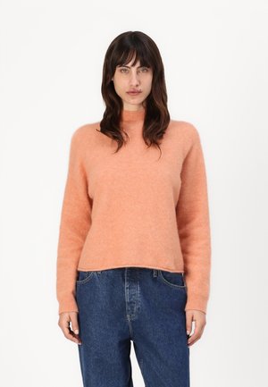 Myk, korallfarget genser med høy hals og lange ermer, med en avslappet passform. Kombinert med blå høytaljede jeans for kontrast.
