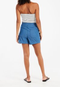 Blue chambray shorts with an elastic waistband and two back pockets, worn with a black and white striped strapless top. Flat sandals.