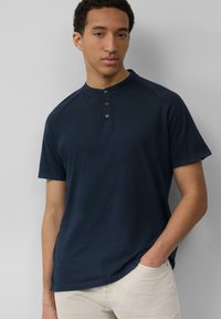 Marineblauwe T-shirt met korte mouwen, ronde halslijn en drieknopenlijst; gemaakt van zacht stof met een gladde textuur.