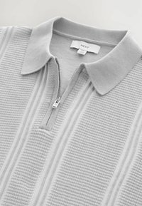 Polo shirt grigio in maglia con colletto con cerniera, caratterizzato da un motivo testurizzato e strisce a coste alternate. L'etichetta riporta "NEXT."