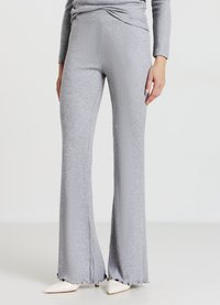 Pantalon évasé en maille côtelée grise avec une coupe ajustée et des détails subtils d'ourlet effiloché, associé à des talons blancs pointus.