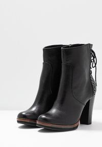 Stivaletti neri in pelle con punta tondeggiante, chiusura con zip e dettagli in pizzo decorativi sul retro. Presentano un tacco a strati e un accento in legno.