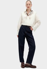 White button-up shirt with large collar, paired with dark blue high-waisted jeans. The outfit includes brown leather shoes and a patterned scarf.