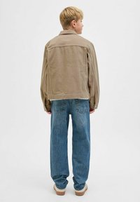 Beige farmerdzseki, laza szabással, látható varrásokkal és gombos záródással, világoskék egyenes szárú farmernadrággal és bézs cipővel párosítva.