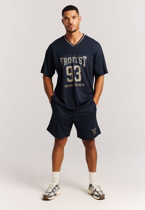 Donkerblauw sportoutfit bestaande uit een mesh shirt met korte mouwen met de opdruk "Protest 93" en bijpassende korte broek, met een ontspannen pasvorm.