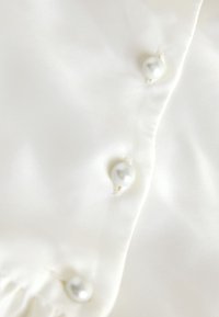 Close-up of a white satin fabric with three pearl buttons sewn along a seam.