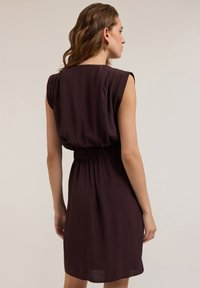 Kurzes ärmelloses Kleid mit taillierter Passform aus dunkelviolettem Stoff. Glatte Textur, knielang, mit geraffter Taille und plissierten Schultern.