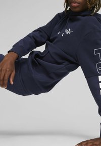 Sudadera de color azul marino hecha de una tela suave, con un bolsillo tipo canguro, capucha con cordón y un logo blanco en el pecho y la manga.