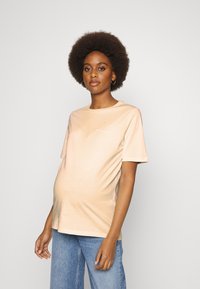 T-shirt de maternidade em pêssego claro com mangas curtas, corte descontraído e detalhe de logotipo pequeno no peito. Tecido suave em mistura de algodão.