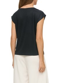 Zwart kortemouwtop met een relaxed fit, gladde textuur en ronde halslijn; gecombineerd met lichtgekleurde, wijde broek.