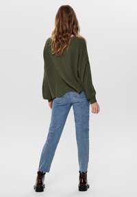Pull en tricot vert olive surdimensionné avec manches amples, associé à un jean en denim bleu clair. Le jean présente des bords effilochés et est fuselé.