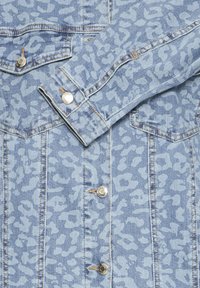 Veste en jean bleu clair avec un motif léopard discret, boutons en métal et coutures visibles aux poignets et aux poches.