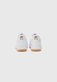 Valkoiset Nike Air -lenkkarit, joissa on teksturoitu kumipohja, pehmustettu nilkkapanta ja kontrastivärinen oranssi swoosh-logo kantapäässä.