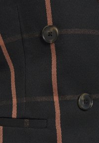 Czarna tkanina z drobnym wzorem w kratkę w kolorze rdzy, z dwoma guzikami i małą kieszonką po lewej stronie. Teksturowane wykończenie.