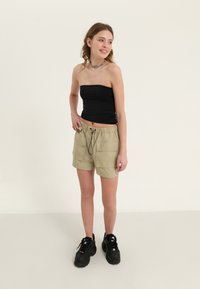 Khaki cargo shorts med elastisk midje, to frontlommer og svart snøring. Båret med en svart stroppeløs topp og svarte sneakers.