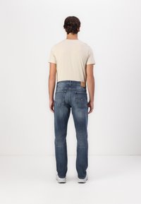 Jean bleu délavé avec une coupe slim, cinq poches et des détails de couture horizontale subtils. Associé à un t-shirt beige clair.