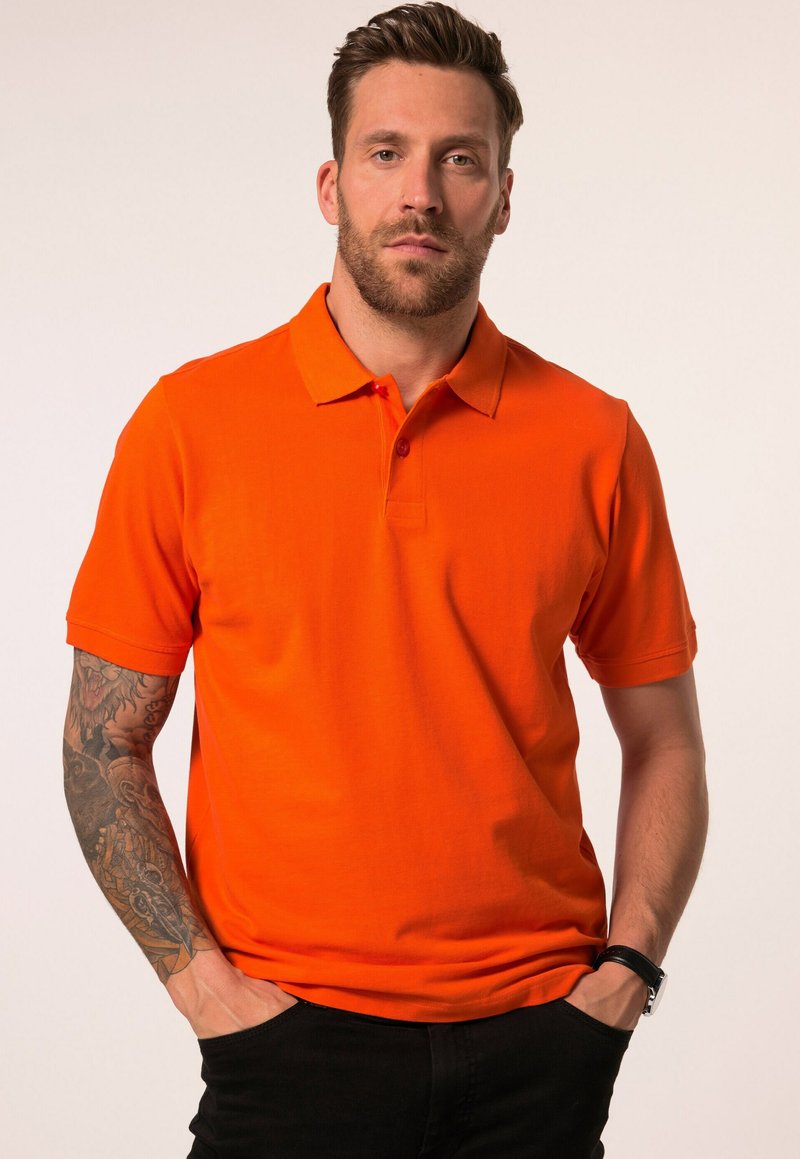 T-Shirt mit kurzen Ärmeln in leuchtendem Orange, aus Baumwolle, mit einem Kragen und einer Knopfleiste mit drei Knöpfen. Das Modell trägt schwarze Hosen.