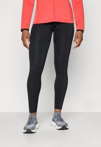 Sorte treningsleggings laget av stretchstoff, kroppsnær design, glatt tekstur, kombinert med grå joggesko og en rød jakke.