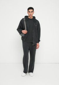 Sudadera con capucha gris oscuro y cremallera frontal, combinada con un cuello redondo texturizado a juego y pantalones de corte relajado; zapatillas blancas; bolso cruzado gris.