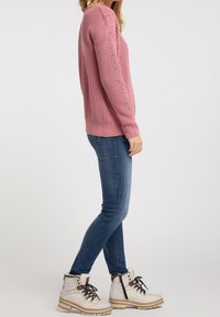 Růžový pletený svetr s texturovaným vzorem, kulatým výstřihem a žebrovanými manžetami, kombinovaný s modrými džíny a bílými šněrovacími botami s kožešinovou podšívkou.