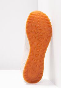 Vit sneakers med en texturerad gummisula i orange. Slät ovandel med sömmar. Varumärket "Skechers" präglat på sulan.