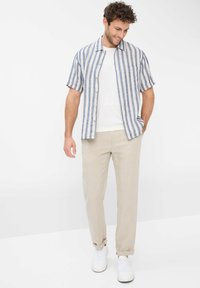 Short-sleeve shirt in blue and white vertical stripes, paired with light beige trousers and white sneakers. Smooth fabric with buttons.