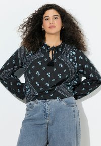 Blusa negra con patrones florales azules, cuenta con un cuello con cordón y mangas globo, combinada con jeans de mezclilla de tiro alto en azul claro.