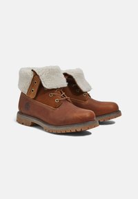 Braune Lederstiefel mit einem künstlichen Fellkragen, Schnürdesign und geriffelter Gummisohle. Auffälliges Logo an der Seite und Kontrastnähte.