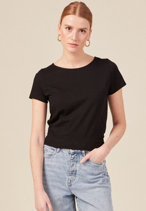 Zwarte top met korte mouwen van zachte stof, met een ronde hals en een iets cropped pasvorm, gecombineerd met lichtblauwe high-waisted jeans.