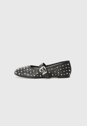 Chaussure noire plate ornée de clous en argent, dotée d'une sangle avec boucle. La chaussure a un bout pointu et un petit talon.
