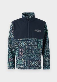 Fleece puslinis megztinis su tamsiai mėlyna viršutine dalimi ir raštuota apatine dalimi žalsvų, mėlynų, rožinių atspalvių, su užtrauktuku ir logotipo detale.