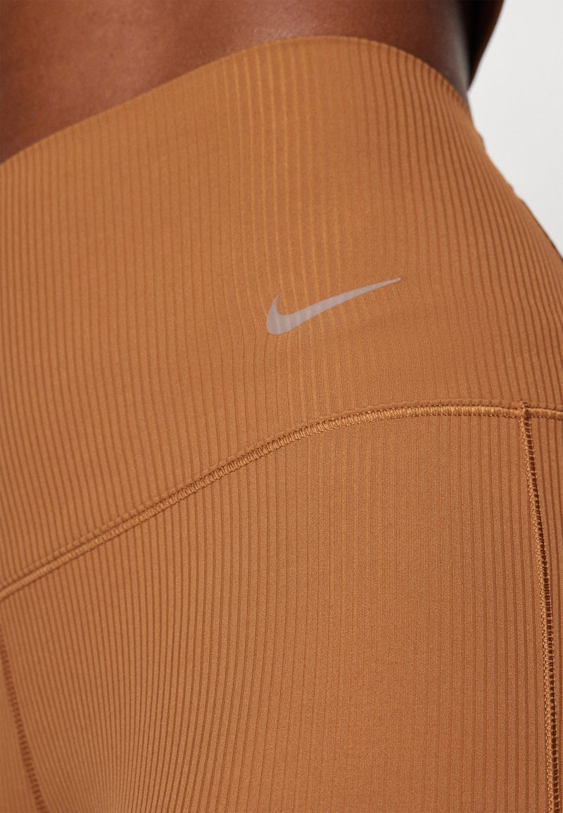 Leggings Nike in una calda tonalità marrone, caratterizzati da una texture a coste, vita alta e dettaglio del logo in colore a contrasto.