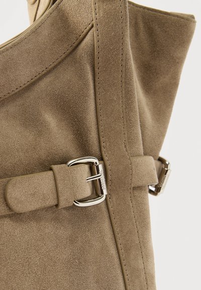 Μπεζ καφέ σουέντ μποτάκι με κάθετη ράβδο και ασημένια αγκράφα, σε απλό φόντο.