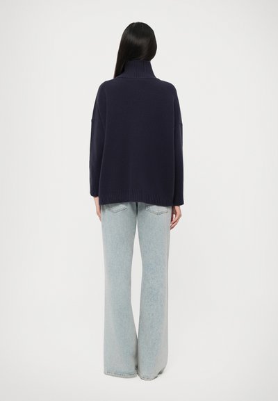Navy turtleneck sweater with loose fit, ribbed hem, and dropped shoulders, paired with light blue wide-leg jeans. Soft knit texture.
