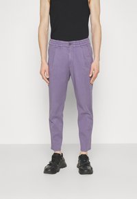 Fialové bavlněné kalhoty s zúženým střihem, předními sklady a knoflíkovým zapínáním. Černé tenisky dotvářejí celý outfit.