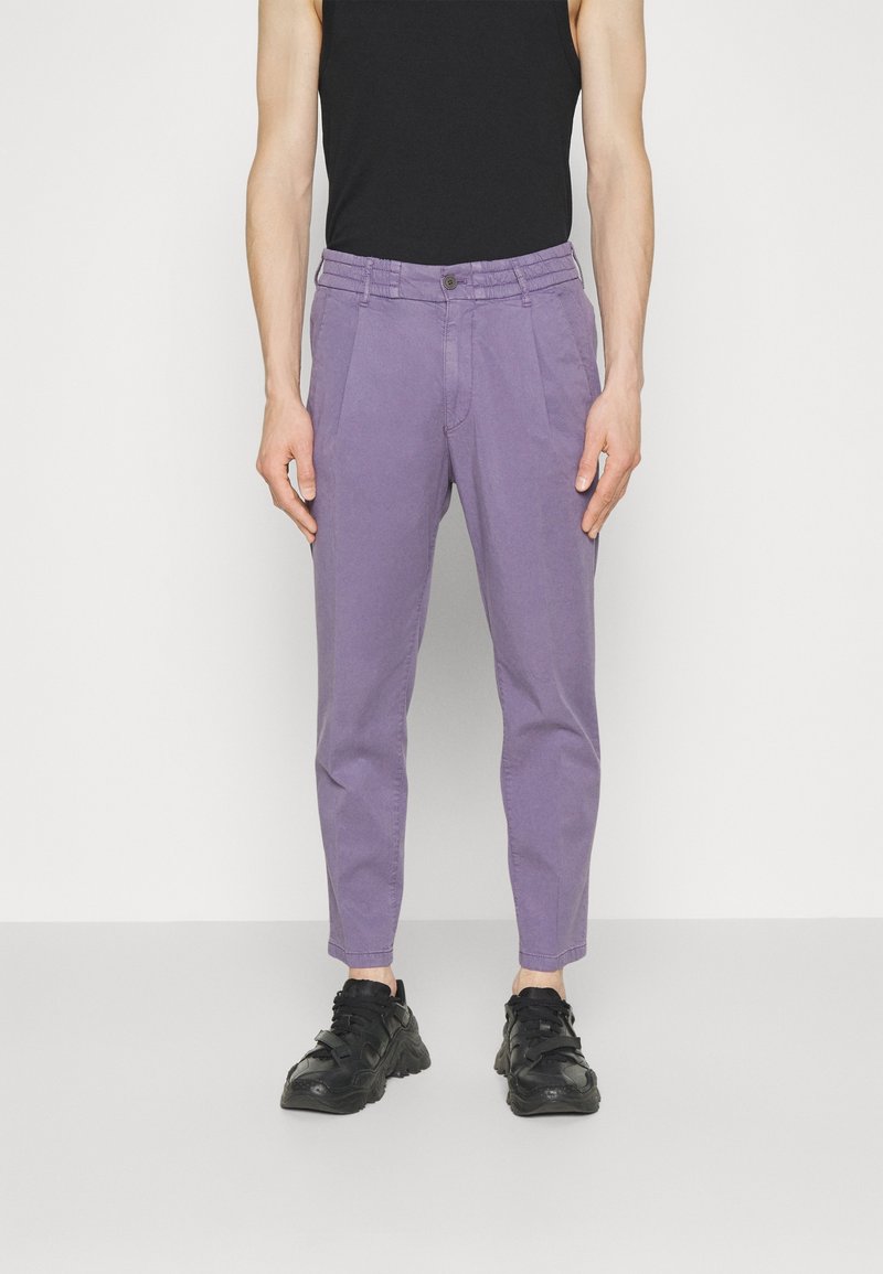 Fialové bavlněné kalhoty s zúženým střihem, předními sklady a knoflíkovým zapínáním. Černé tenisky dotvářejí celý outfit.