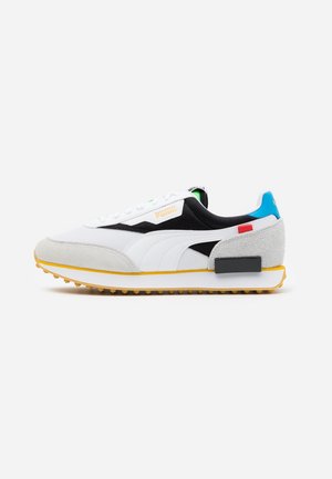 Weißer, schwarzer und grauer Puma-Sneaker mit gelber Sohle und blauem Fersenakzent, von der Innenseite auf weißem Hintergrund dargestellt.