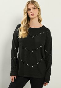 Maglione lungo nero a maniche lunghe con scollo rotondo, tessuto a trama e inserti decorativi bianchi disposti in un motivo a chevron.