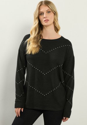 Maglione lungo nero a maniche lunghe con scollo rotondo, tessuto a trama e inserti decorativi bianchi disposti in un motivo a chevron.