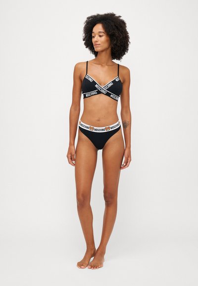 Black bralette and bikini set with cross straps and logo band. Soft, stretchy fabric with a smooth texture. Features a cartoon bear logo on waistband.