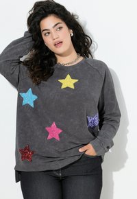 Ciemnoszary sweatshirt o luźnym kroju, z kolorowymi aplikacjami w kształcie gwiazd z cekinów w odcieniach różu, żółci, niebieskiego i fioletowego na przodzie.