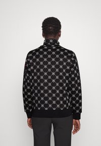 Black sweater featuring a repeating white circular logo pattern, high collar, ribbed cuffs, and hem. Smooth texture, casual fit.