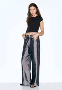 Crni kratki top sa srebrnim zakovicama; široke hlače metalik sive boje s prednjim džepovima; model nosi crne sandale na petu.