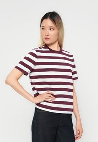 Camiseta de manga corta a rayas en color marrón y blanco con cuello redondo, que presenta un corte relajado y un tejido suave. Se lleva con jeans oscuros.