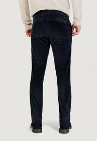 Pantaloni in velluto a coste blu navy con vestibilità slim, caratterizzati da costine verticali, due tasche posteriori e gambe leggermente affusolate. Scarpe in pelle completano il look.