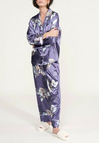 Ensemble de pyjama en satin violet avec un motif floral, top à manches longues et pantalon ample. Des pantoufles blanches douces et duveteuses complètent la tenue.