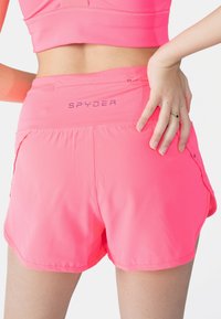 Pantalones deportivos rosas hechos de tela ligera, con un logo en la cinturilla, bolsillos laterales y un diseño suave y aerodinámico.